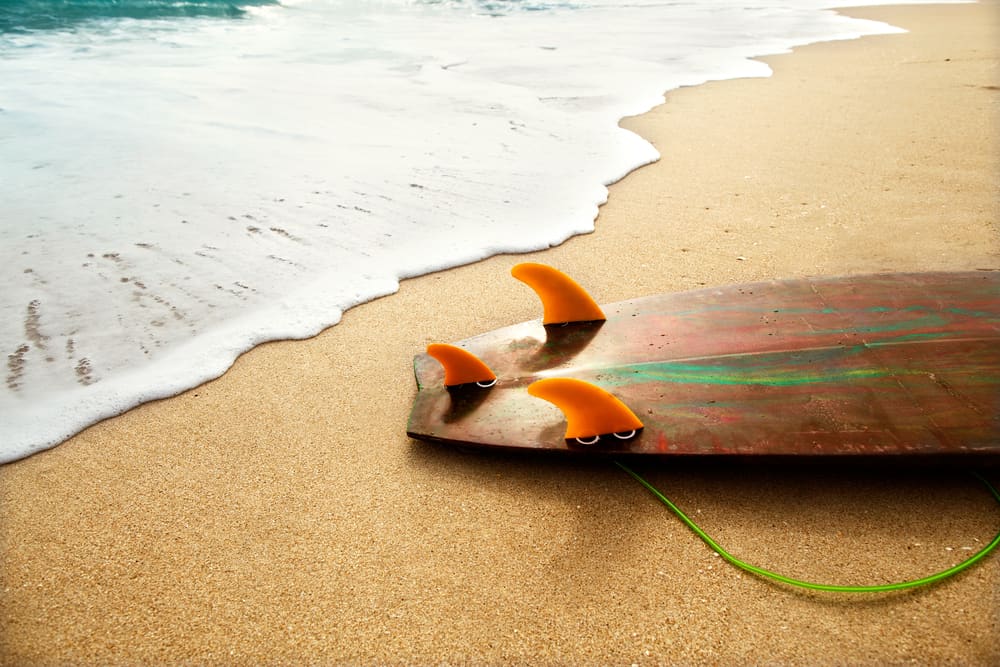 Fins on the end of a surfboard on the beach at the edge of the water