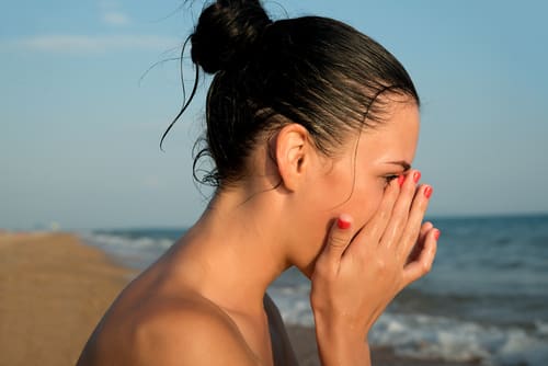 women standing at the beach rubbing her irritated eyes
