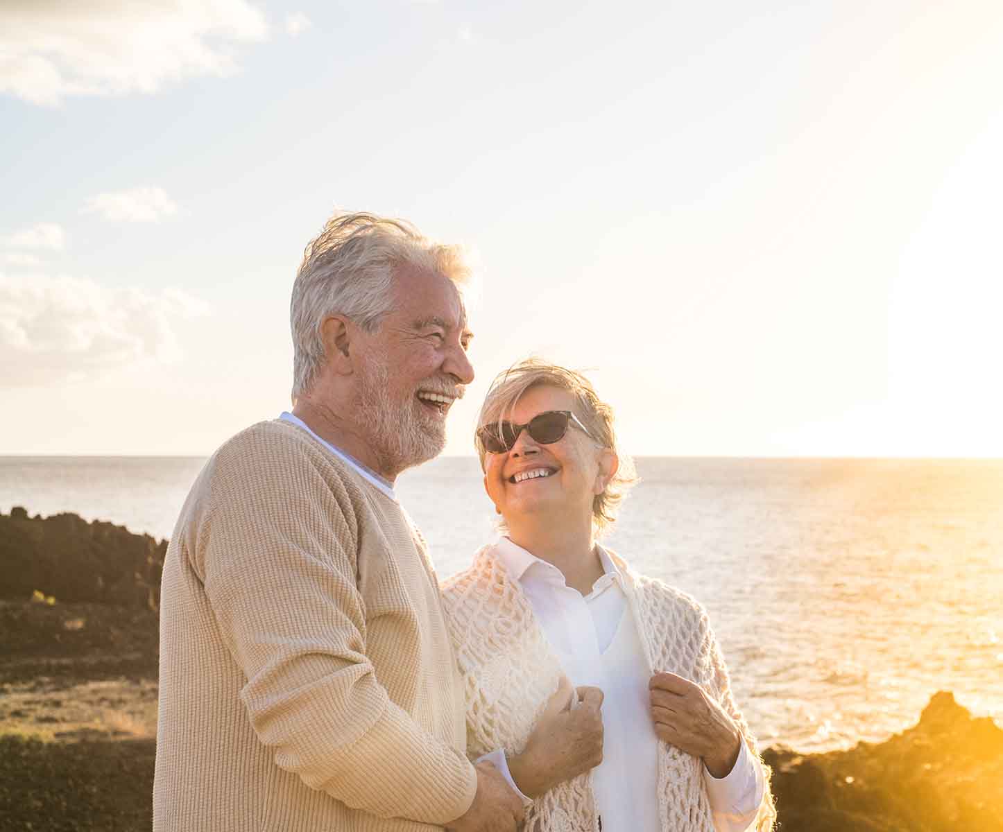 happy older couple smiling at the beach during sunset